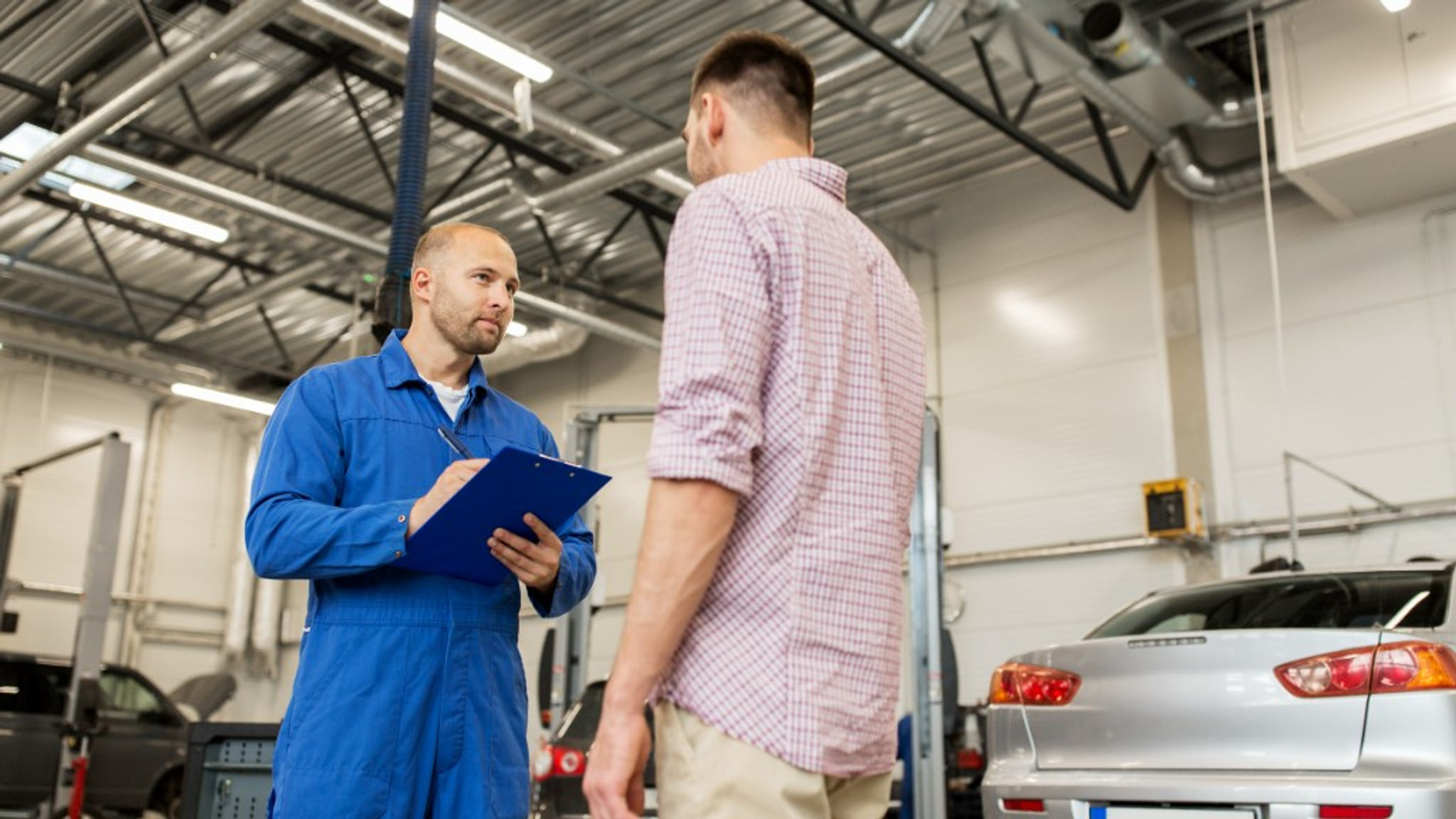 Mechanic with a clipboard talking through work with a customer in the workshop